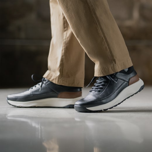 The image features a model wearing tan pants and black Men’s casual shoes on a white floor. Shop the Men’s Casual Shoes category now. 