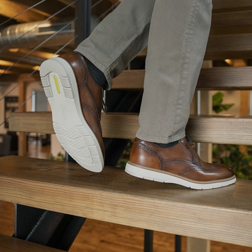 The image features a model walking up wooden steps while wearing brown Men’s hybrid shoes. Shop the Men’s Hybrid Shoes category now.