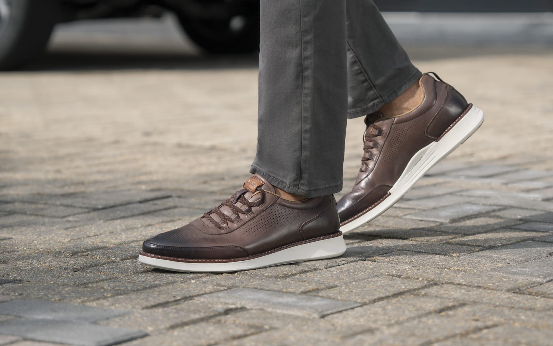 Image features the Launch Elastic Lace Slip On in brown on a cobbled street.